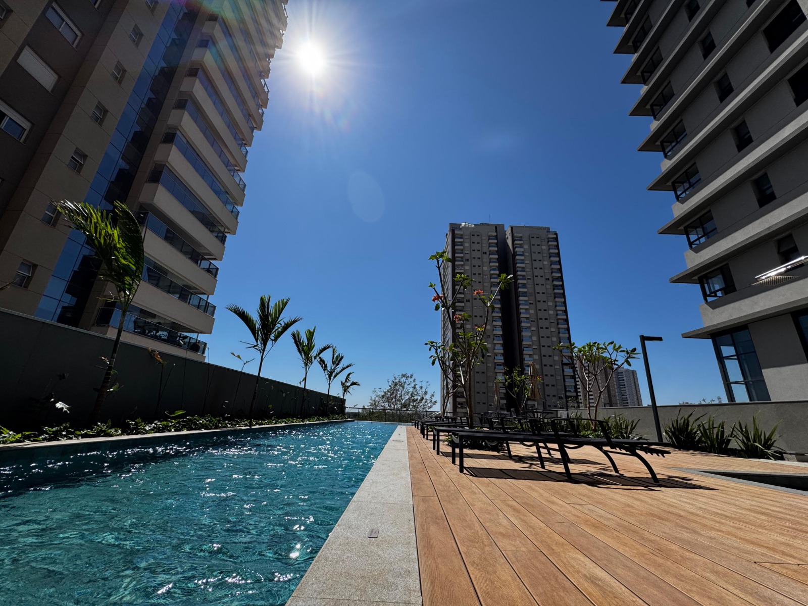 Piscina do condomínio com deck de madeira e espreguiçadeiras